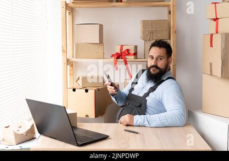 Propriétaire indien de petite entreprise utilisant l'application mobile sur smartphone en vérifiant la boîte à colis. Employé d'entrepôt, vendeur tenant téléphone faire la livraison de dépôt de détail Banque D'Images