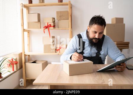 Entrepreneur de démarrage de l'homme millénaire indien avec boîte pour l'emballage de commande de shopping en ligne travaillant à la maison de bureau, le propriétaire de petite entreprise de fabrication Banque D'Images