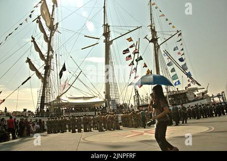 Jeunes femmes portant un parapluie et un appareil photo, alors qu'elles marchent sur le quai, dans un fond de KRI Dewaruci (Dewa Ruci), un grand navire indonésien, qui est ouvert aux visiteurs publics au port de Kolinlamil (port de la Marine) à Tanjung Priok, dans le nord de Jakarta, Jakarta, Indonésie. Banque D'Images