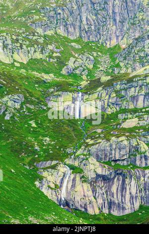 Cascade naturelle située dans les montagnes colorées de la Suisse, au milieu de la végétation animée du col de Furka en été. Structure en pierre. Banque D'Images