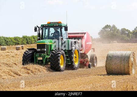 Un agriculteur local conduit son tracteur John Dere et sa presse à balles pour recueillir et mettre en balles du blé de paille coupé pour le stockage de la litière pour animaux et l'utilisation générale de la ferme en hiver. N Banque D'Images