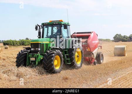 Un agriculteur local conduit son tracteur John Dere et sa presse à balles pour recueillir et mettre en balles du blé de paille coupé pour le stockage de la litière pour animaux et l'utilisation générale de la ferme en hiver. N Banque D'Images