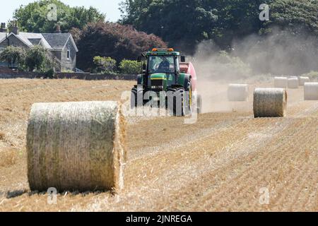 Un agriculteur local conduit son tracteur John Dere et sa presse à balles pour recueillir et mettre en balles du blé de paille coupé pour le stockage de la litière pour animaux et l'utilisation générale de la ferme en hiver. N Banque D'Images