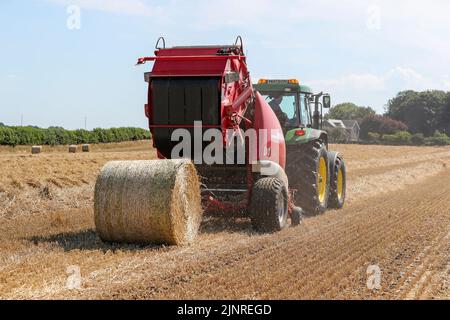 Un agriculteur local conduit son tracteur John Dere et sa presse à balles pour recueillir et mettre en balles du blé de paille coupé pour le stockage de la litière pour animaux et l'utilisation générale de la ferme en hiver. N Banque D'Images