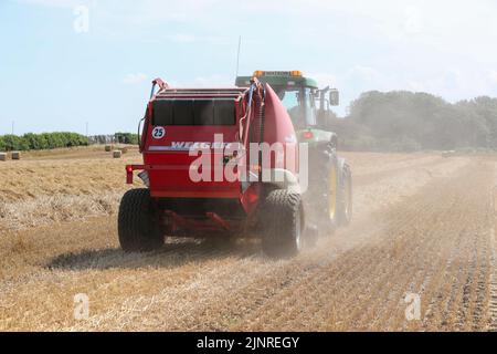 Un agriculteur local conduit son tracteur John Dere et sa presse à balles pour recueillir et mettre en balles du blé de paille coupé pour le stockage de la litière pour animaux et l'utilisation générale de la ferme en hiver. N Banque D'Images