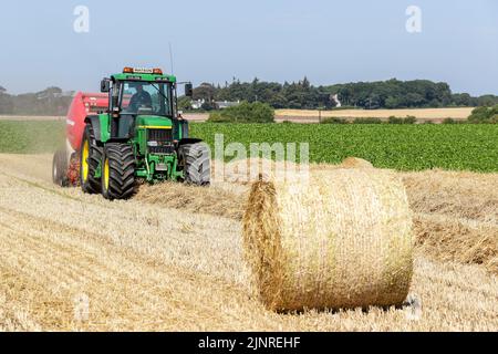 Un agriculteur local conduit son tracteur John Dere et sa presse à balles pour recueillir et mettre en balles du blé de paille coupé pour le stockage de la litière pour animaux et l'utilisation générale de la ferme en hiver. N Banque D'Images