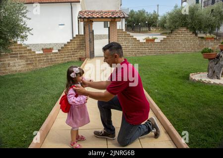 Image d'un jeune père préparant sa fille pour la première journée d'école. Petite fille avec sac à dos et tablier rose. Banque D'Images