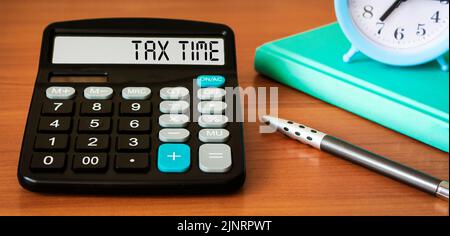 Mot de temps de taxe sur la calculatrice et la table en bois. Concept commercial et fiscal. Moment du paiement d'impôt dans une année. Banque D'Images