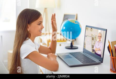 Adorable écolière étudiant en ligne à la maison parlant à une enseignante senior par appel vidéo. Banque D'Images