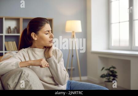 Une femme qui souffre d'un mal de dents fort est assise sur un canapé et touche sa joue Banque D'Images