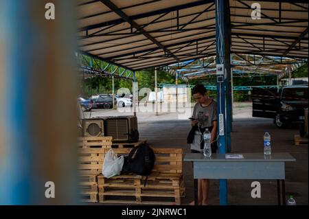 Zaporizhzhia, Ukraine. 13th août 2022. Un jeune homme charge son téléphone alors qu'il attend l'autorisation de retourner dans les territoires occupés russes après s'être enfui plus tôt dans l'invasion. De nombreux Ukrainiens ont tenté de retourner dans les zones occupées pour diverses raisons, notamment pour aider leur famille à venir en aide, pour retourner chez eux ou pour savoir si leur maison se tient encore. (Photo de Madeleine Kelly/SOPA Images/Sipa USA) crédit: SIPA USA/Alay Live News Banque D'Images