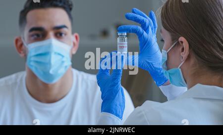 Vue de derrière la cacaise femme méconnaissable le médecin porte des gants médicaux tient le pot avec le médicament du vaccin contre le virus Covid-19 montre l'homme espagnol arabe Guy Banque D'Images