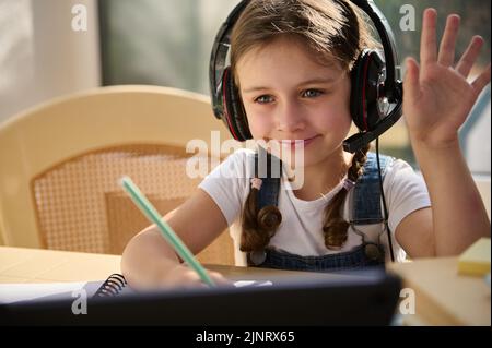 Gros plan d'un élève du primaire intelligent, portant un casque audio, souriant tout en regardant une leçon vidéo en ligne Banque D'Images