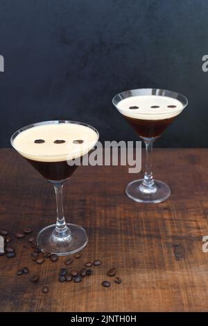 Verres de martini expresso avec grains de café sur table en bois et fond noir Banque D'Images