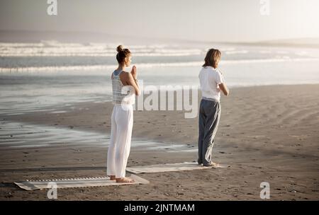 Le cadre idéal pour un calme parfait. Un jeune couple pratiquant le yoga ensemble sur la plage. Banque D'Images