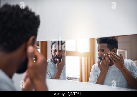 Garder un œil sur sa peau. Un beau jeune homme examinant son visage dans un miroir dans la salle de bains à la maison. Banque D'Images