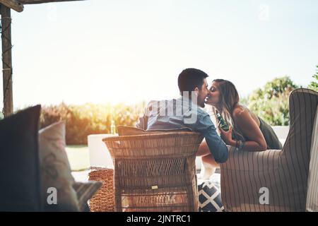 Les meilleurs sièges de la maison. Photo d'un jeune couple affectueux qui embrasse tout en dégustant des bières sur leur patio. Banque D'Images