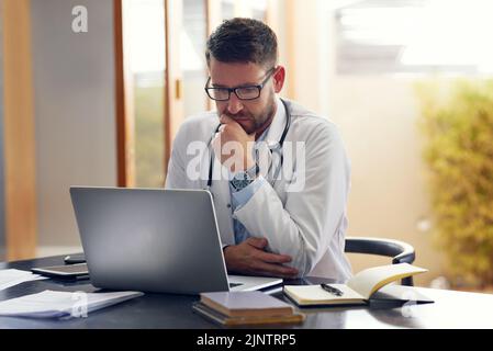 Les dossiers médicaux sont la clé d'une bonne santé. Un beau médecin masculin travaillant sur son ordinateur portable tout en étant assis dans son bureau. Banque D'Images