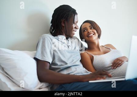Vous trouverez toujours quelque chose de drôle à rire en ligne. Un jeune couple qui s'attend à utiliser un ordinateur portable ensemble tout en se relaxant au lit à la maison. Banque D'Images