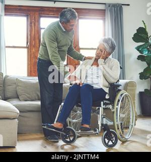Tout sera bien mon amour, je vous le promets. Une femme âgée qui a l'air inquiète assise dans un fauteuil roulant tout en étant soutenue et tenue par son mari Banque D'Images