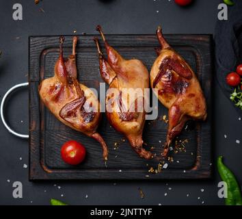 La friture des carcasses de cailles repose sur une planche en bois avec des légumes, une table noire Banque D'Images