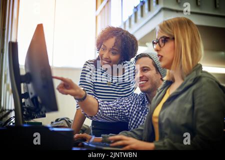 Theyve s'est associée pour leur prochain projet. Un groupe d'étudiants universitaires travaillant ensemble sur un ordinateur dans la bibliothèque du campus. Banque D'Images