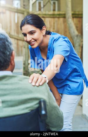 Comment allez-vous aujourd'hui, monsieur. Une jeune infirmière gaie tenant l'épaule d'un patient dans un fauteuil roulant pour le soutien à l'extérieur à la maison. Banque D'Images