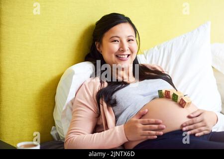 La maternité est une si belle bénédiction. Portrait d'une femme enceinte couchée avec des blocs de bois pour bébé sur son ventre à la maison. Banque D'Images