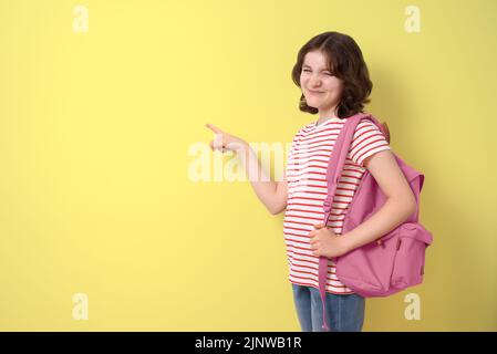 Bonne écolière avec sac à dos, pointant vers l'espace de copie, sur fond jaune Banque D'Images