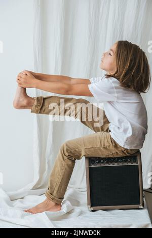 S'ennuient une jeune fille assise sur un ampli de guitare, redressant sa jambe en tenant ses orteils Banque D'Images