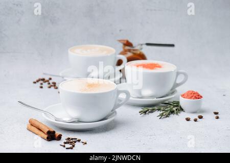 Cappuccino d'image à faible angle avec crème et épices dans trois tasses sur soucoupes sur une surface de table. Décoration avec ajout d'ingrédients. Banque D'Images