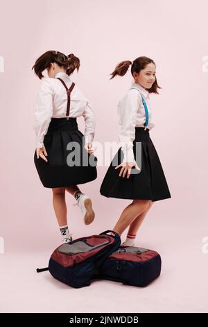 Dansant deux filles d'école avec deux queues dos à dos. Les sacs à dos sont empilés au premier plan. Porter des uniformes d'école avec des jupes et des bretelles hautes pour les genoux Banque D'Images