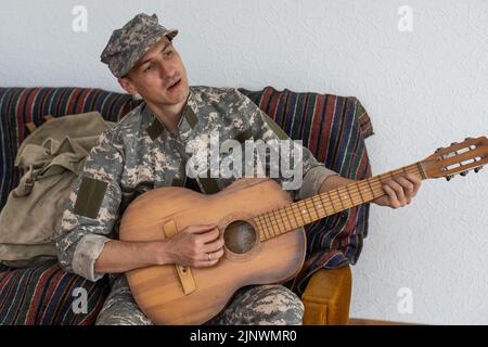 Vétéran du concept de jeu de guitare en fauteuil roulant. Réunion de famille. Fils et femme. Uniforme de camouflage. Contexte familial. Se reposer ensemble. Des sentiments qui se manifestent Banque D'Images