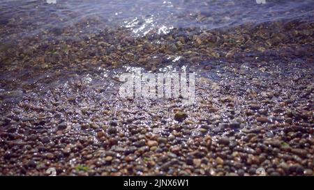 Gros plan sur la plage de galets avec des vagues transparentes et un reflet du soleil sur l'eau. Gros plan sur la côte rocailleuse. Fond naturel d'une mer calme dans le surf Banque D'Images