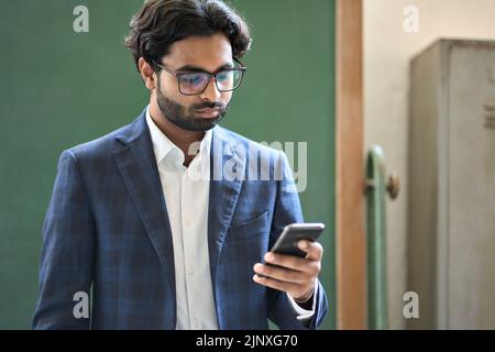 Jeune homme d'affaires indien utilisant un smartphone travaillant debout au bureau. Banque D'Images