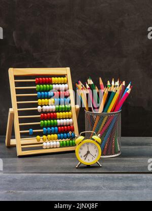 Retour à l'école. Crayons colorés, Abacus maths et réveil sur bureau bleu, fond de tableau noir, espace de copie Banque D'Images