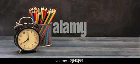 Il est temps pour la bannière de l'école. Crayons colorés et réveil sur le bureau en bois bleu de la salle de classe, fond de tableau noir, espace de copie Banque D'Images