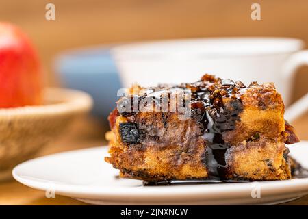 Gros plan une tranche de gâteau maison aux fruits versée avec du sirop de chocolat sur un plat en céramique blanc avec une pomme mûre rouge dans un panier en bambou et une tasse de coff Banque D'Images