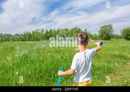 Un garçon d'âge préscolaire souffle de grosses bulles de savon dans un champ lors d'une journée ensoleillée Banque D'Images