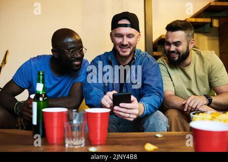 Jeune homme avec un smartphone montrant des photos de sa famille à ses amis ou communiquant par chat vidéo tout en ayant du bon temps ensemble Banque D'Images