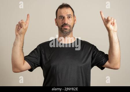 Portrait d'un latin barbu heureux pointant les doigts vers le haut à l'espace de copie isolé sur fond beige. Banque D'Images