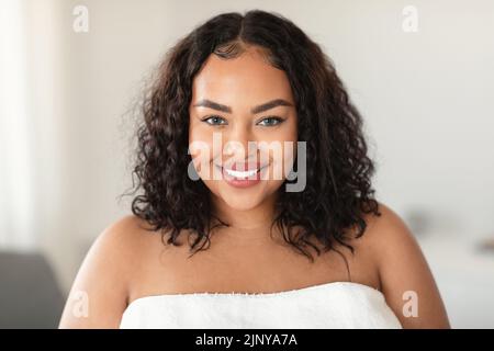 Portrait de beauté de la grande dame afro-américaine debout enveloppée dans une serviette et souriant à l'appareil photo Banque D'Images