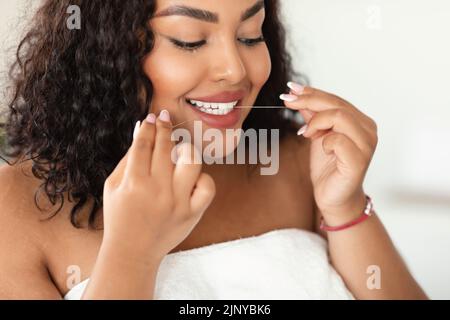 Concept de soins buccaux. Jeune femme noire plus grande taille utilisant la soie dentaire, nettoyage parfait des dents blanches, gros plan Banque D'Images