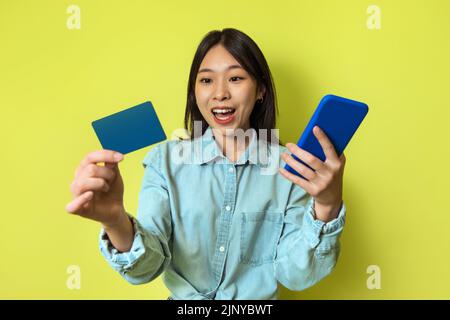 Korean Lady Holding téléphone et carte de crédit Shopping en ligne, Studio Banque D'Images