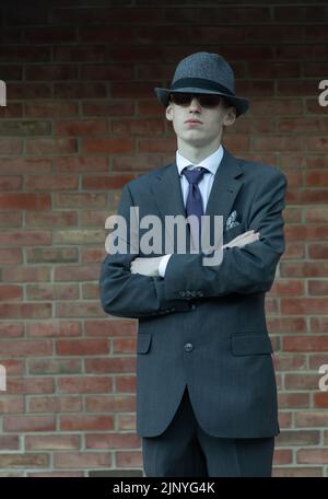 Portrait d'un jeune homme en costume, bras croisés, avec chapeau et lunettes de soleil Banque D'Images