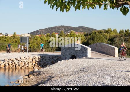 Vodice, Croatie - 19 juillet 2022: Personnes à vélo et à pied sur une passerelle côtière avec un pont Banque D'Images