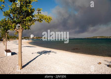 Vodice, Croatie - juillet, 13th 2022: Plage vide et fumée de l'été feu de forêt se rapprochant de la ville. Banque D'Images