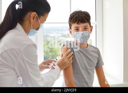 Garçon d'école dans le masque médical se faire vacciner pour le protéger pendant une pandémie Banque D'Images