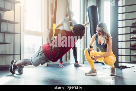 Femme et homme à l'entraîneur de harnais dans la salle de gym Banque D'Images