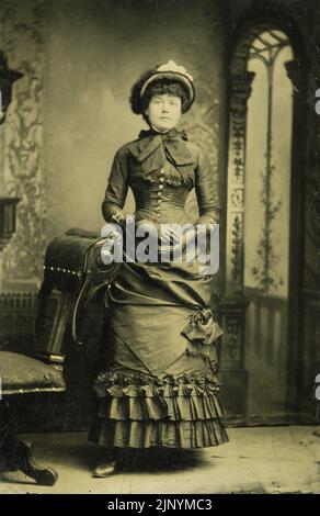 Studio photo fin 19th siècle Portrait d'une femme formelle sérieuse debout dans des vêtements d'époque avec toile de fond vers 1870 - 1880s Banque D'Images